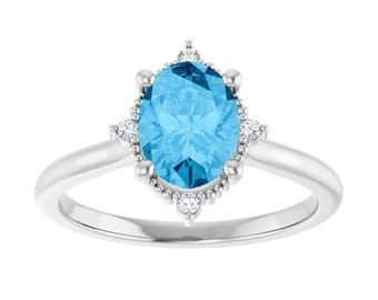 May include: A silver ring with a large, oval-cut, light blue gemstone. The gemstone is encircled by smaller, clear stones and a decorative silver setting. The ring's band is a simple, polished silver.