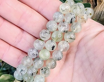 May include: A bracelet made of clear green and black gemstone beads. The beads are round and have a smooth, polished finish.