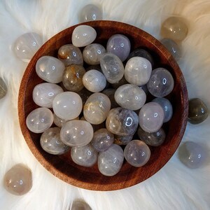 May include: A wooden bowl filled with translucent white and gray tumbled stones. The stones are smooth and polished, with a variety of shapes and sizes.