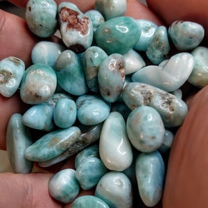 May include: A collection of tumbled blue and green ocean jasper stones. The stones are smooth and polished, with a variety of patterns and colors.