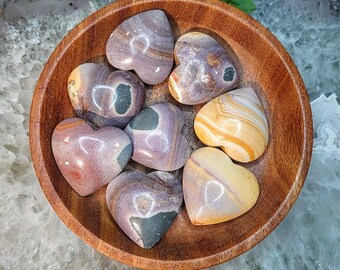 May include: A collection of eight heart-shaped polished stones in a wooden bowl. The stones are in shades of pink, purple, brown, and yellow with swirling patterns.