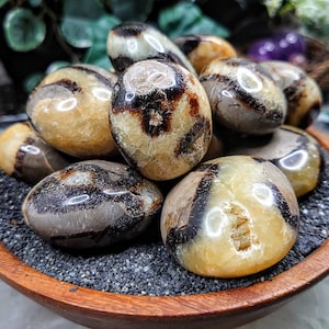 Op de afbeelding: Een verzameling gepolijste, bruin-gele gebande agate stenen in een houten kom. De stenen zijn glad en hebben een natuurlijke, organische uitstraling.