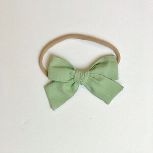 May include: A light green fabric bow headband for babies and toddlers. The headband is made of a soft, stretchy material and is perfect for everyday wear.