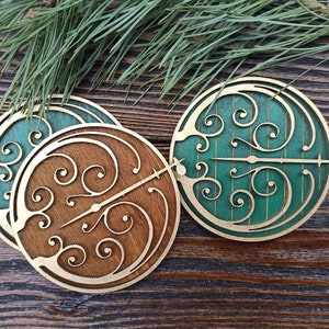 May include: Three wooden coasters with a green and brown swirling design. The coasters are round and have a cutout in the center.