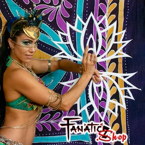 May include: A woman wearing a gold and green costume holds a white, decorative, lotus-shaped prop. The prop is made of wood and has a delicate, intricate design. The background is a colourful fabric with a floral pattern.