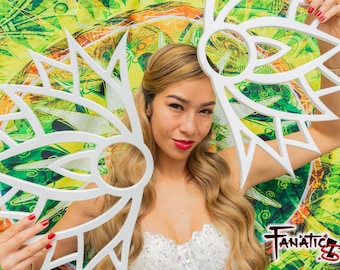 May include: A woman holds two white, geometric, decorative wall hangings in front of a colorful, patterned background. The wall hangings are shaped like stylized flowers with multiple points.