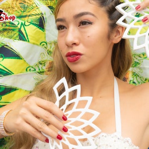 Op de afbeelding: Een vrouw met lang blond haar houdt twee witte, decoratieve, geometrische, bloemvormige stukken vast. De stukken zijn gemaakt van een lichtgewicht materiaal en hebben een delicaat, ingewikkeld ontwerp. De vrouw draagt een wit topje met pailletten en rode lippenstift.