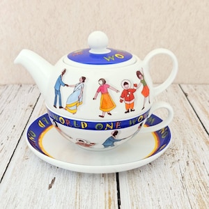 May include: A white ceramic tea set for one featuring a teapot that stacks onto a teacup and saucer. The set is decorated with colorful illustrations of diverse people and the repeating text "WORLD ONE WORLD" in blue and yellow bands.