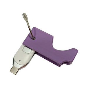 Op de afbeelding: Een paarse plastic sleutelhangerhouder met een zilveren metalen lus en een witte USB-stick eraan bevestigd.