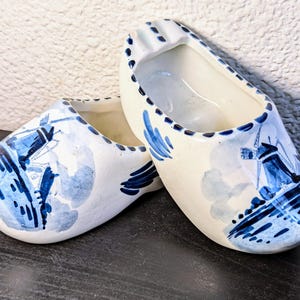 May include: Two blue and white ceramic Dutch shoe planters with windmill designs. The planters are empty and ready for plants.