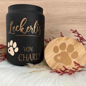 May include: Black ceramic jar with a gold paw print and the text "Leckerlis von CHARLY". The jar has a bamboo lid with a gold paw print.