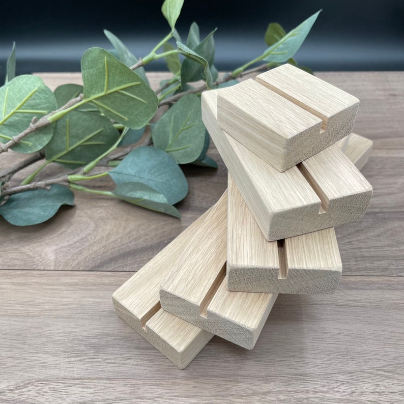 Pu&ograve; includere: Un gruppo di blocchi di legno chiaro con una fessura nella parte superiore. I blocchi sono disposti ad angolazioni diverse, con un rametto di foglie verdi sullo sfondo. Il legno presenta una venatura naturale.