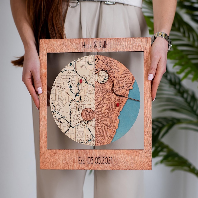 A woman holds a personalized wooden circle map keepsake with two connected locations and an established date engraved below. This photo shows an alternative round style within the collection for couples who want a custom engagement or wedding display piece.