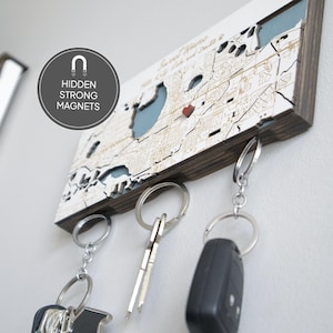 May include: Wooden key holder with a map design, featuring a blue lake and a red heart. The key holder has a dark brown frame and silver key rings. The text "Sweet Home" is visible on the map. The text "Hidden Strong Magnets" is also visible.