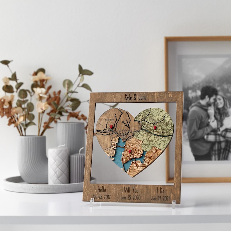 A dark wood framed heart puzzle map sits on a shelf beside flowers and a framed black-and-white couple photo. This image presents the personalized wedding gift as sentimental decor tied to real places and milestones.