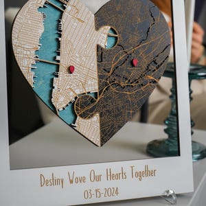 Close-up of a white-framed wooden heart map showing two connected locations, layered wood detail, and red place markers. This image focuses on the symbolic heart design and the fine map engraving that make the keepsake feel special.