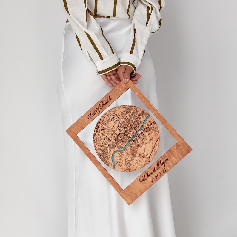 May include: A square wooden frame featuring a circular laser-engraved map with a blue river detail. The frame is inscribed with the text Scott & Michele and Where it all began 10-21-2023. The wood has a natural light brown finish.