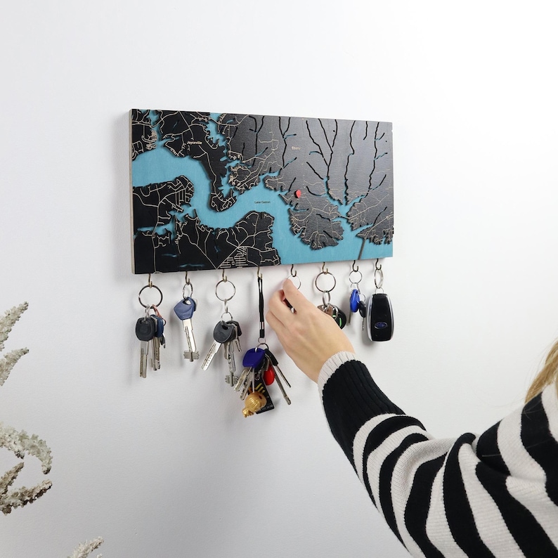 A person reaches for keys on a dark wood map key rack mounted on a white wall. This custom entryway organizer shows how the wall key holder works for everyday use in a modern home.