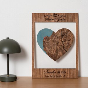 May include: A wooden heart-shaped map with a blue background and a red pin marking a location. The map is framed in a wooden frame with the text "Andrew & Josline" and "November 16, 2024 Cuvier Park in La Jolla, CA" engraved on the frame.