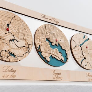 May include: A wooden wall display featuring three circular laser-cut maps with teal water details and red location pins. The top horizontal bar is engraved with "Thomas and Lizzy," while the bottom bar displays "Dating 4.27.2021," "Engaged 12.15.2023," and "Married 5.31.2024."