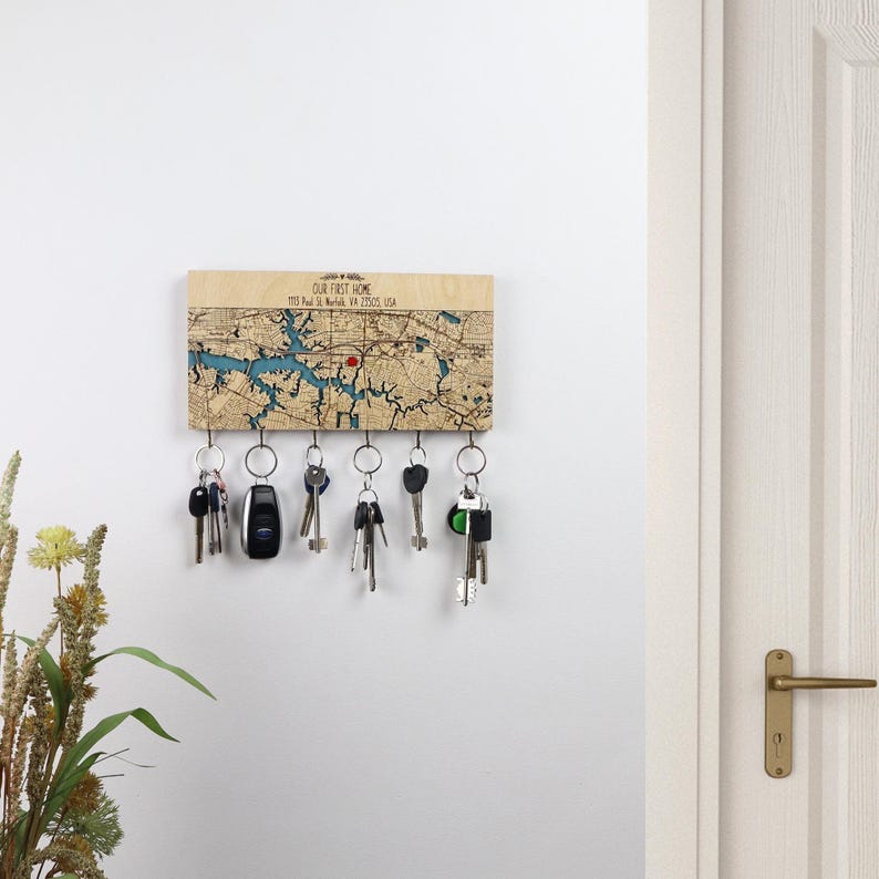 A light wood custom map key holder is displayed on a bright entryway wall near a door and dried greenery. The piece works as modern wall storage that keeps daily keys visible and easy to grab.