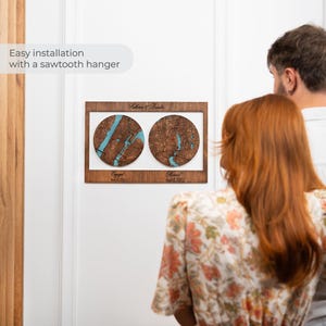 May include: A rectangular wooden wall plaque featuring two circular map inlays with blue water details. The top text reads Katherine & Brandon, while the bottom text displays Engaged April 15, 2021 and Married April 15, 2023. It includes a sawtooth hanger.