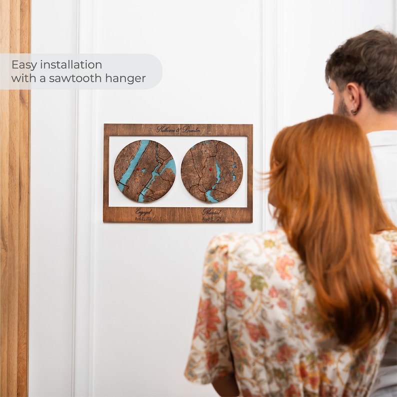 May include: A rectangular wooden wall plaque featuring two circular map inlays with blue water details. The top text reads Katherine & Brandon, while the bottom text displays Engaged April 15, 2021 and Married April 15, 2023. It includes a sawtooth hanger.