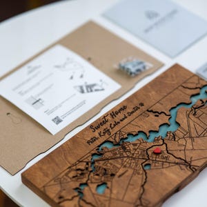 May include: A wooden map with a detailed city layout, featuring a river with blue resin. The map is engraved with the words "Sweet Home" and names. A small red heart marks a location. Includes instructions and hardware.