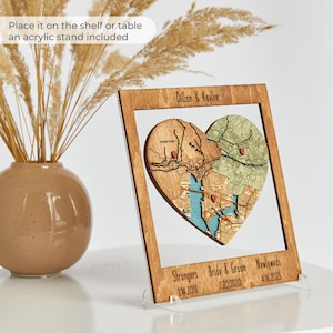 A warm wood framed heart puzzle map is displayed on an acrylic stand beside a ceramic vase, with text noting it can be placed on a shelf or table. This image shows the keepsake as a ready-made wedding gift for a couple that also works as home decor.