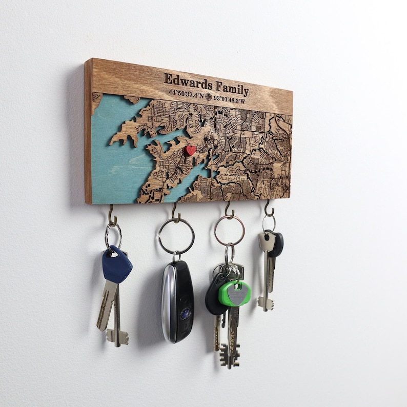 Close-up of a personalized wooden map key rack engraved with a family name and coordinates, holding several keys. This modern wall key holder combines meaningful location detail with practical everyday storage.