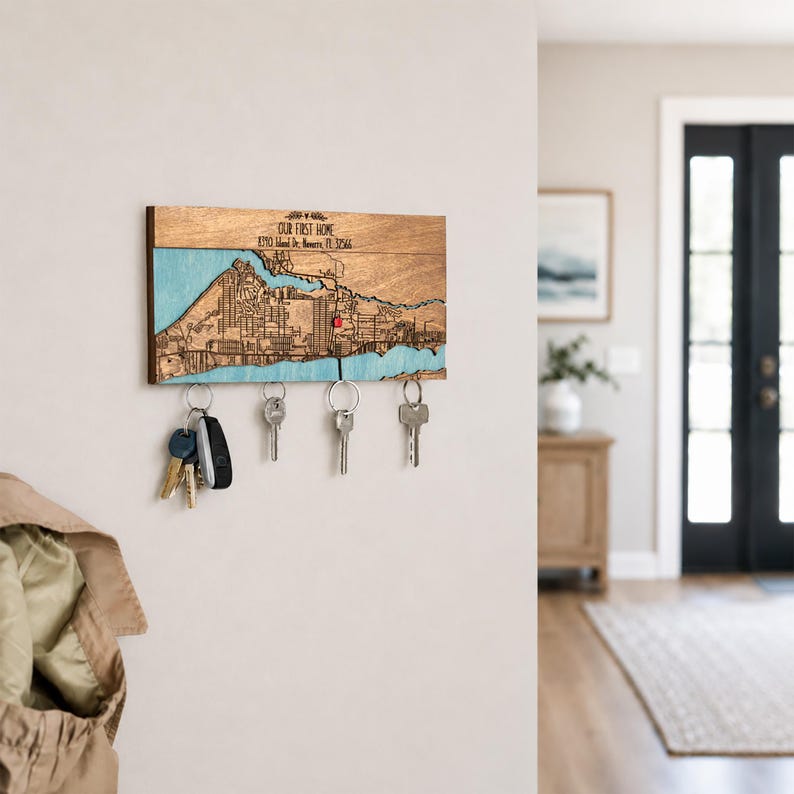 A wall-mounted custom map key organizer is displayed in a clean home entryway with keys held below. This personalized wooden piece works as a practical housewarming gift for a first home.