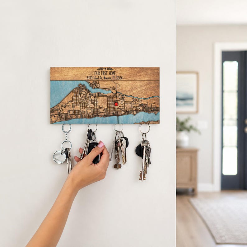 A personalized location map key holder is shown in a bright entryway while a hand reaches for keys. The wooden map organizer keeps daily keys easy to grab near the front door.