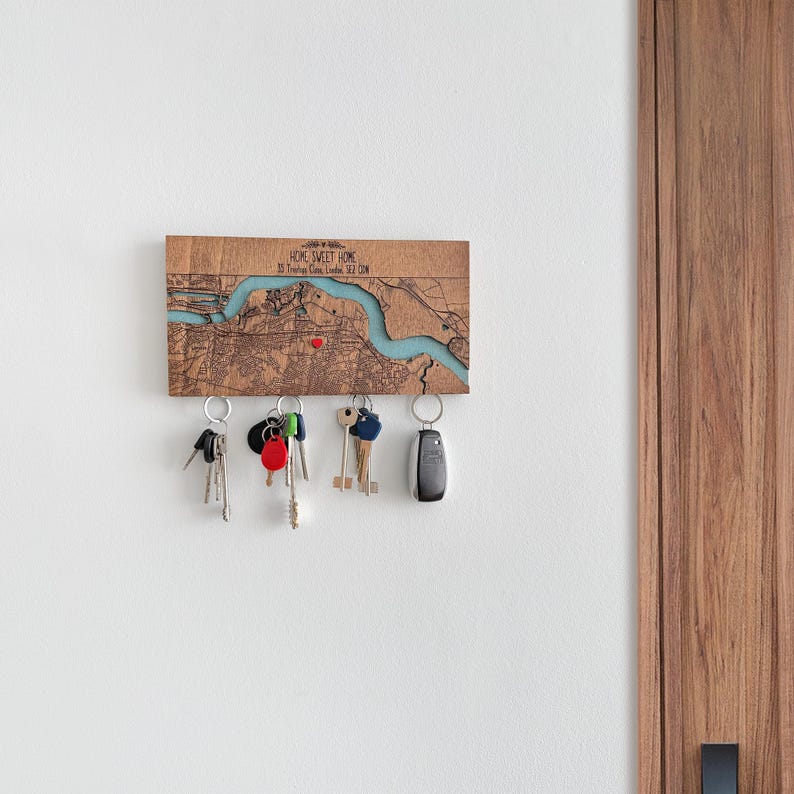 May include: Wooden key holder with a map design, featuring a blue river and a red marker. The key holder has several key rings with keys attached. The text "HOME SWEET HOME" is visible on the top of the key holder.