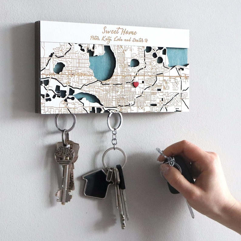 Close-up of a white custom map key holder mounted on a wall with keys held underneath by hidden magnets. The personalized wooden design creates a simple and useful entryway organizer.