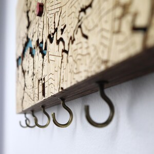 Close-up side view of the sturdy metal hooks under a wooden map key rack. This detail photo highlights the clean construction and functional design for everyday key organization.