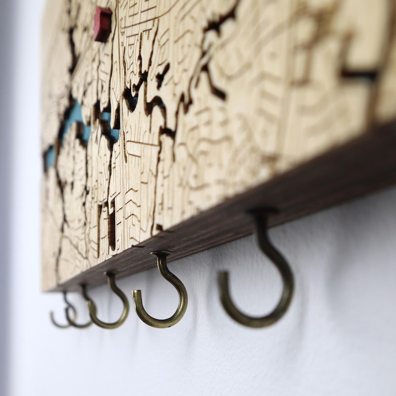 Close-up side view of the sturdy metal hooks under a wooden map key rack. This detail photo highlights the clean construction and functional design for everyday key organization.