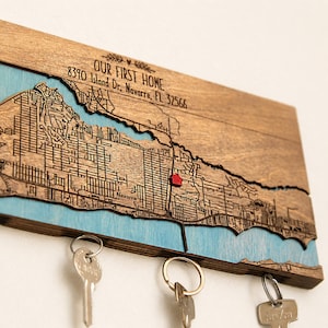 Close-up of the wooden location map showing engraved streets, blue water details, and a red marker for the special address. The hidden magnets below the map hold keys in a simple entryway setup.