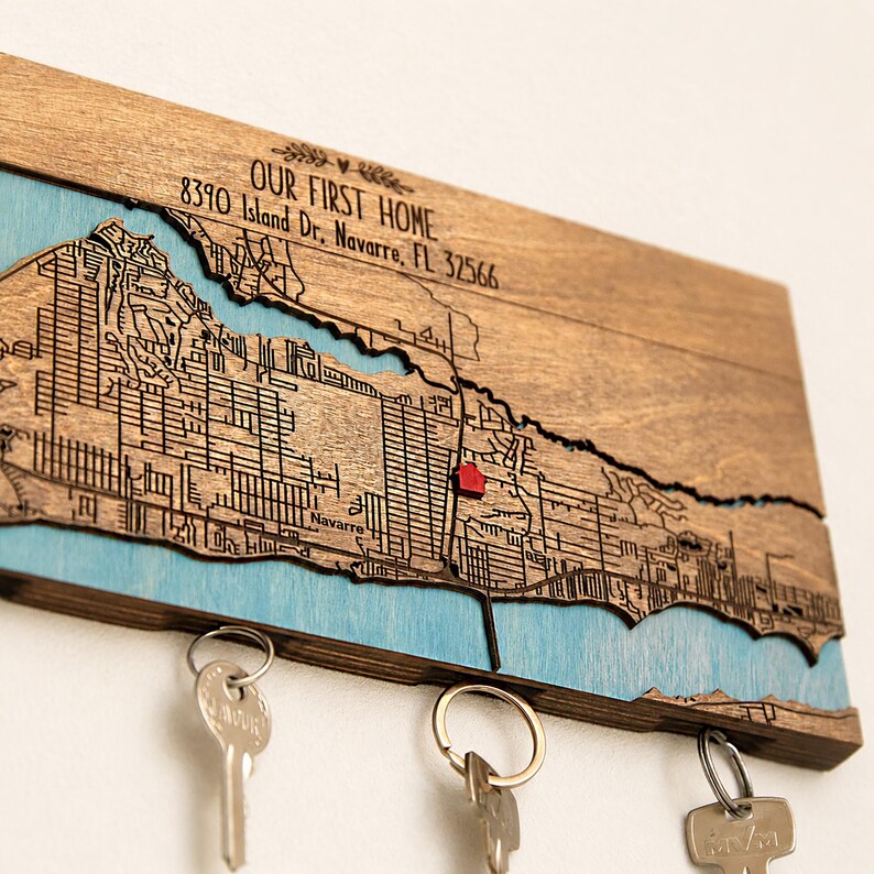 Close-up of the wooden location map showing engraved streets, blue water details, and a red marker for the special address. The hidden magnets below the map hold keys in a simple entryway setup.