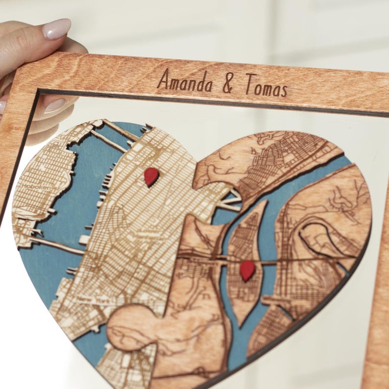 Close-up of a personalized wooden heart map with two location layers, red markers, and engraved names across the top of the frame. This detail shot emphasizes the handcrafted precision and symbolic union behind the custom couple gift.