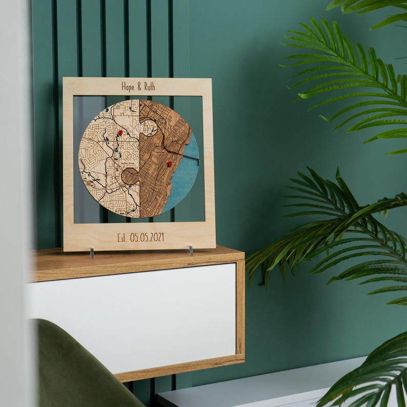 Personalized wooden circle map displayed on a shelf against a deep green wall, with names and an established date engraved on the frame. This image presents the custom couple keepsake as warm, refined decor with strong visual contrast.