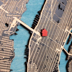 Close-up of the custom wooden map showing the layered street details and the red house icon marking a special address. This image focuses on the craftsmanship and the personalized location detail that makes the first home map unique.