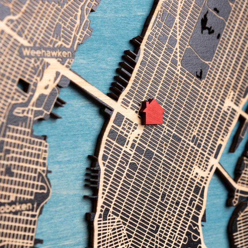 Close-up of the custom wooden map showing the layered street details and the red house icon marking a special address. This image focuses on the craftsmanship and the personalized location detail that makes the first home map unique.