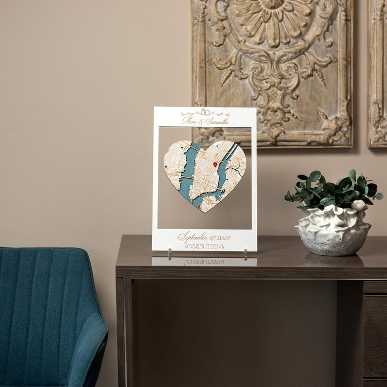May include: A white wooden frame with a heart-shaped map of New York City inside. The map is blue and white with a red pin marking a location. The frame has the text "September 7, 2021" and "New York, NY" printed on it.