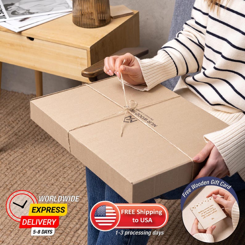May include: A brown cardboard box with a string tied around it. The box is labeled "MUR WOOD HO" and has a logo of a stylized "M". The box is being held by a person's hand. A small wooden gift card is also shown in the image. The gift card has the text "Free Wooden Gift Card" printed on it.