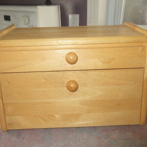 May include: A light wood bread bin with two drawers and rounded edges. The drawers have wooden knobs.