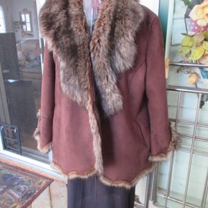 Peut inclure: Un manteau en daim marron avec un col et une garniture en fausse fourrure. Le manteau est suspendu à un support jaune. La garniture en fourrure est un mélange de couleurs marron et beige. Le manteau a un design classique.