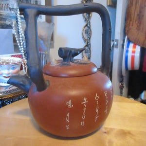 May include: A white ceramic mug with a black handle and the text "But First, Coffee" in a bold, black font. The mug is set against a blurred background, suggesting a cosy setting.
