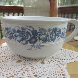 May include: A large white ceramic bowl with a blue and white floral design. The bowl has a wide rim and a single handle.
