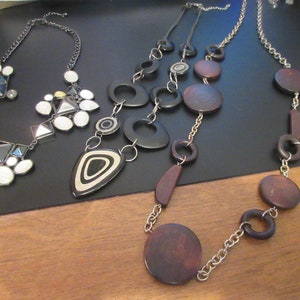 May include: Three necklaces with different styles and colours. One necklace has white and black geometric shapes, another has brown and black wooden circles, and the third has brown wooden circles and ovals.