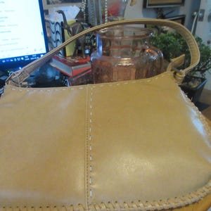 May include: A light brown leather handbag with a stitched edge and a braided strap.